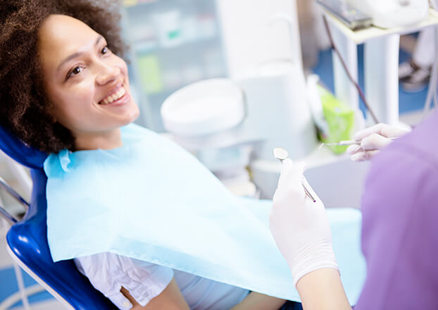 woman sitting in a dental chair as a hygienist prepares to examine her teeth