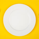 Aerial view of a white place on a yellow background flanked with a fork and knife
