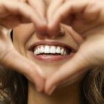 Closeup of a woman holding her hands in a heart shape in front of her white smile after professional teeth whitening